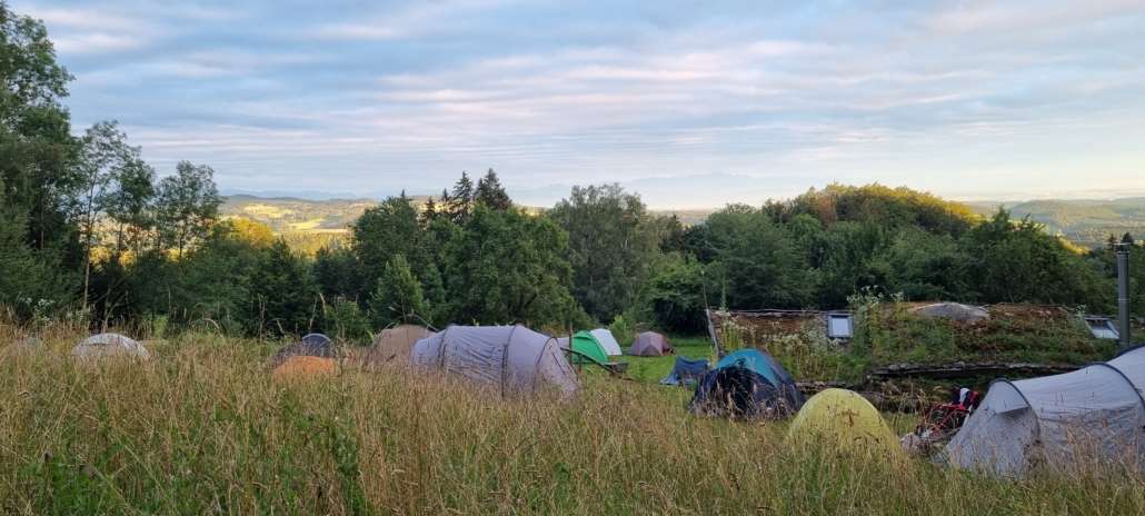 Bunte Zelte in einer Wiesen-Wald-Hügellandschaft